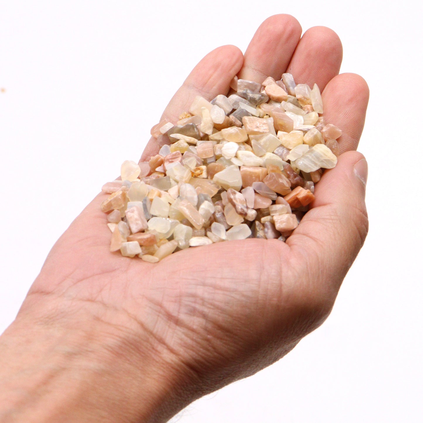 Hand holding polished natural moonstone gemstone chips in various soft colors by SGI Online SGI Online