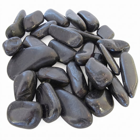 A pile of smooth, polished black tumbled stones, likely river rocks or spa stones, arranged on a plain white background. SGI Online