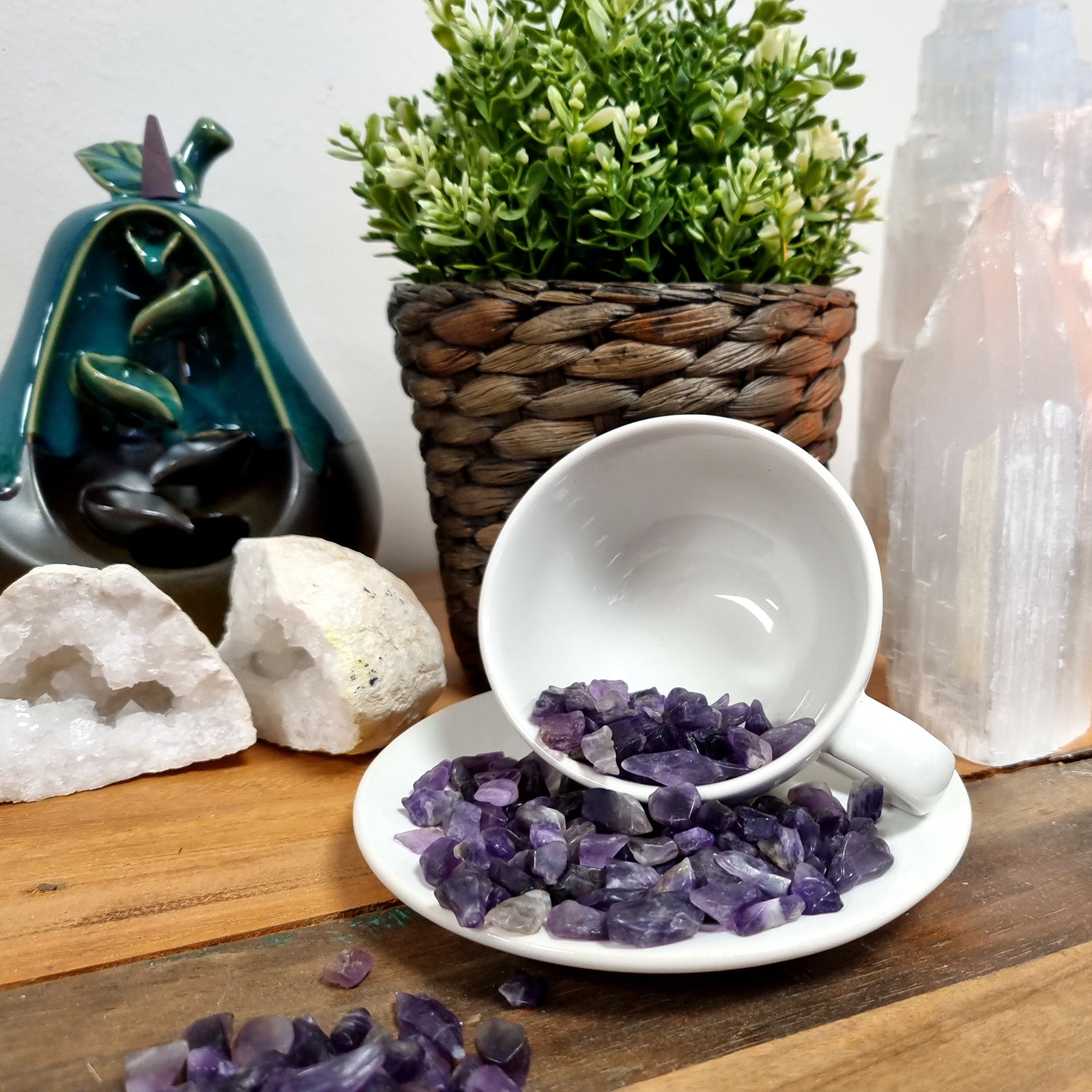 SGI Online polished amethyst gemstone chips spilled from a white teacup onto a white saucer on a wooden surface