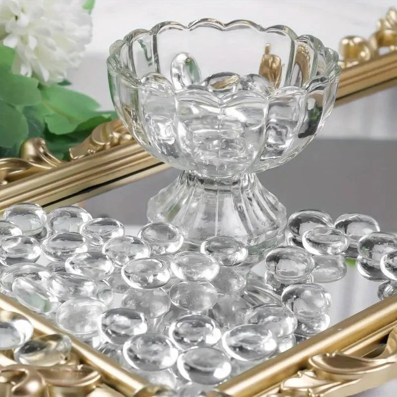 Clear glass pebbles by STONED displayed on a decorative mirror tray with a glass bowl and floral background