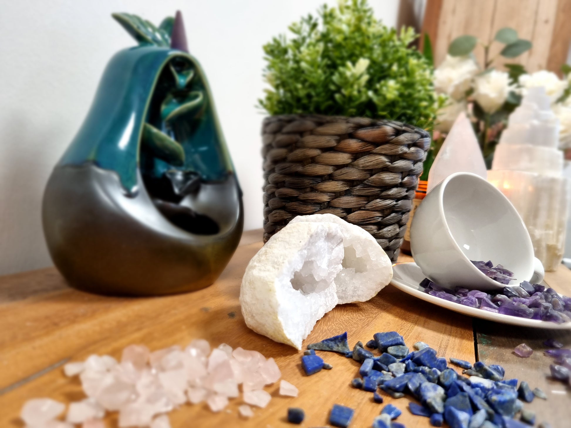 Clear quartz gemstone chips and other polished gemstones displayed on wooden surface with decorative plant and items
