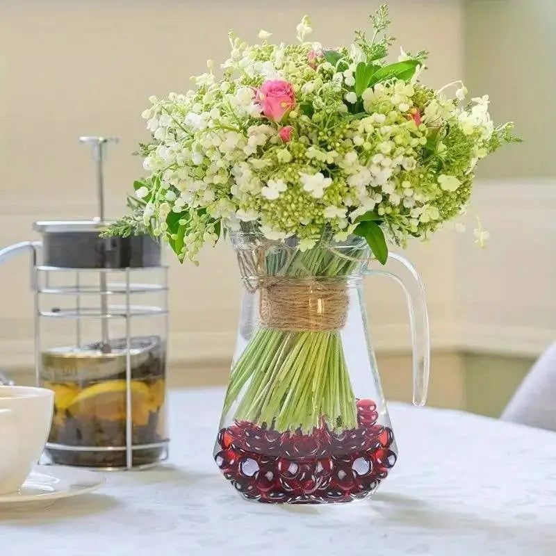 Clear glass pitcher with white and pink flowers arranged over red glass pebbles by STONED