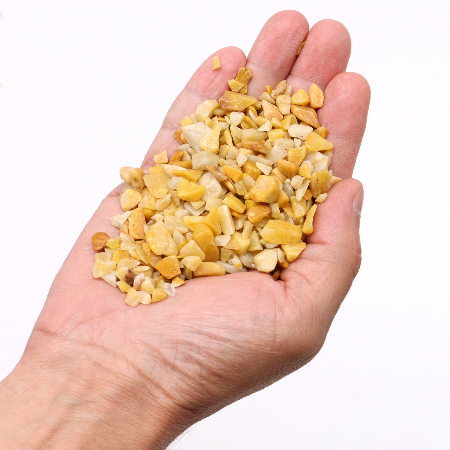 Hand holding polished golden quartz gemstone chips from SGI Online on a white background SGI Online