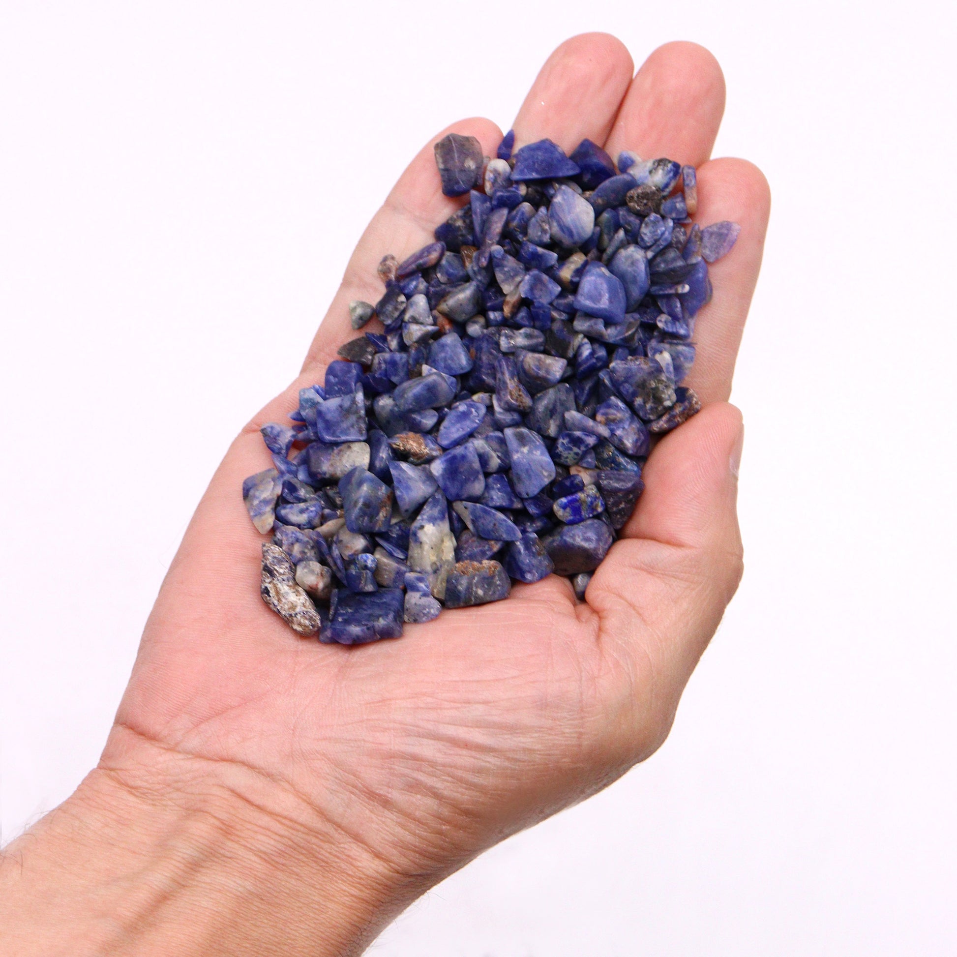 Hand holding polished sodalite gemstone chips for crafts by SGI Online in deep blue and white hues