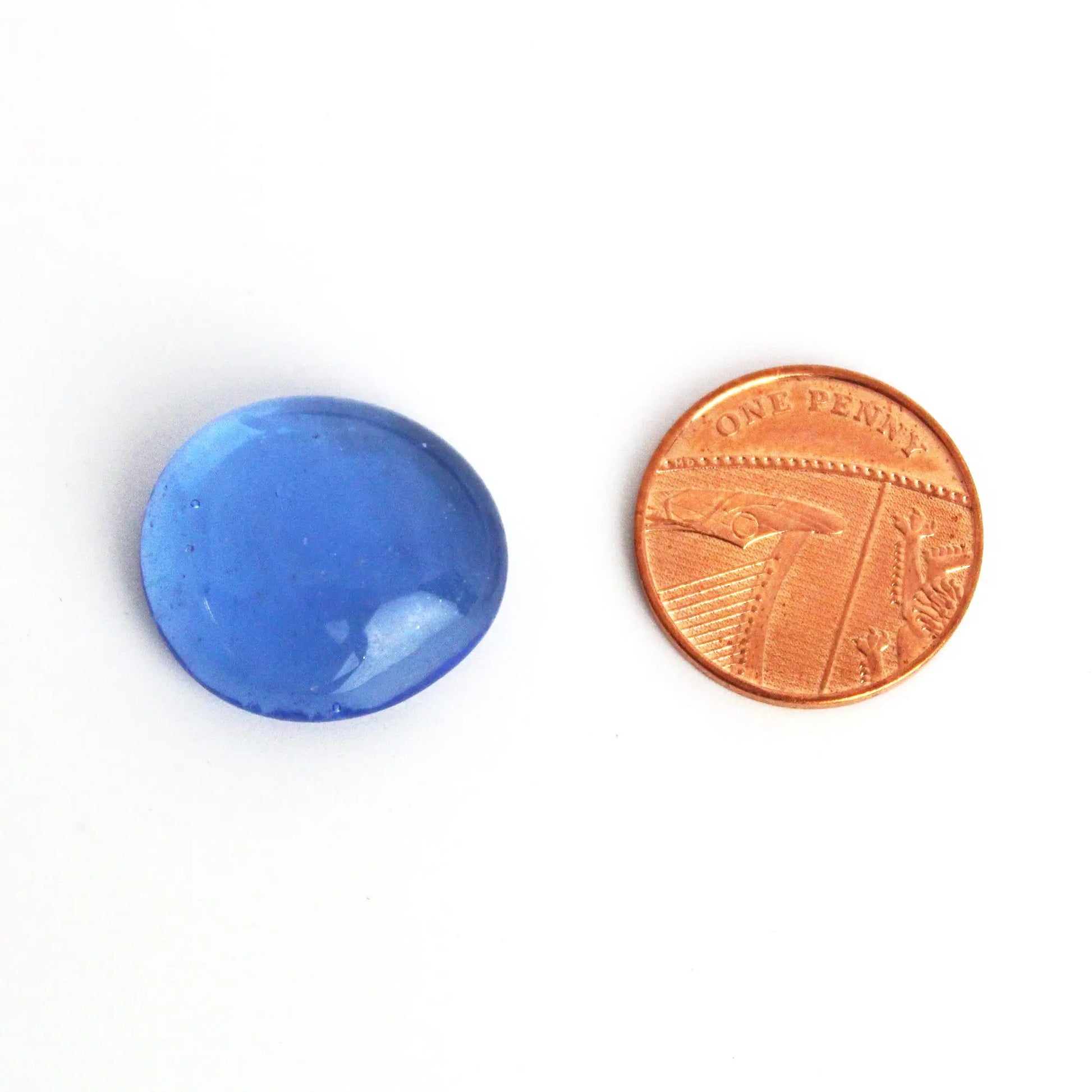 STONED premium blue glass pebbles next to a penny for size comparison on a white background