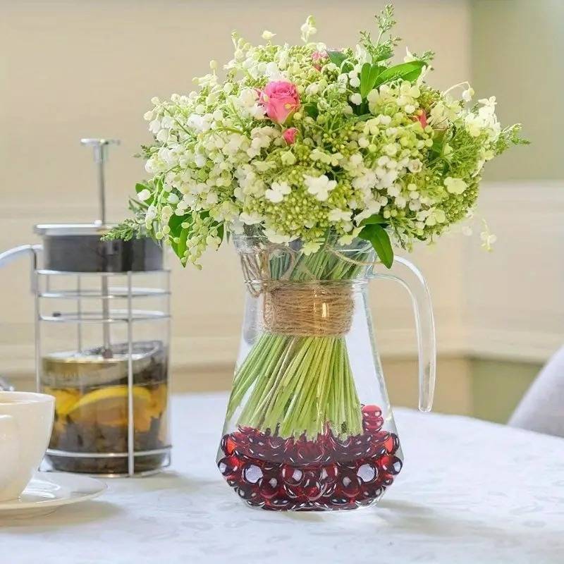 Clear glass pitcher vase with white and pink flowers and red glass pebbles bulk at the bottom
