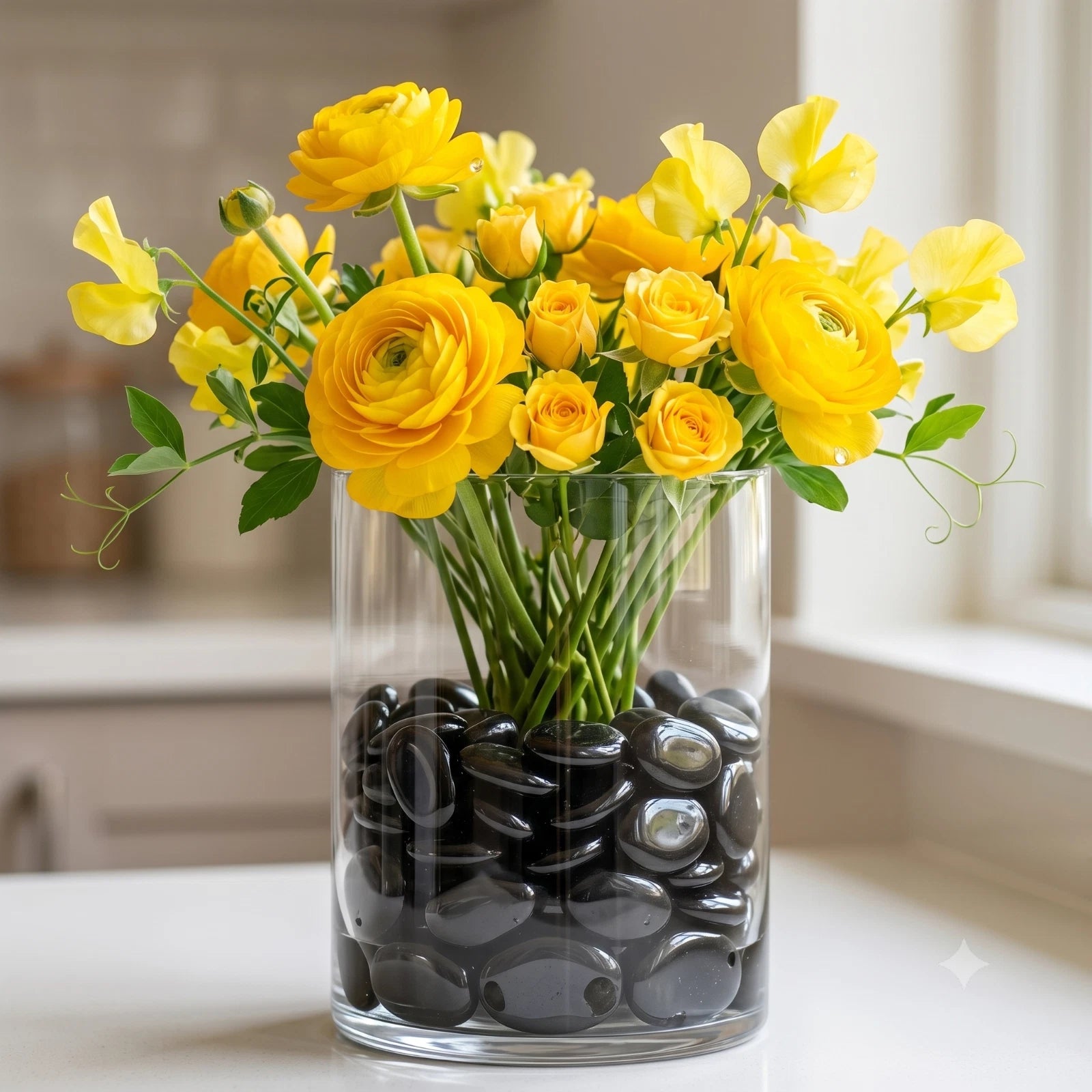 Clear glass vase filled with Black Polished Glass Decorative Pebbles holding yellow ranunculus flowers in bright kitchen setting