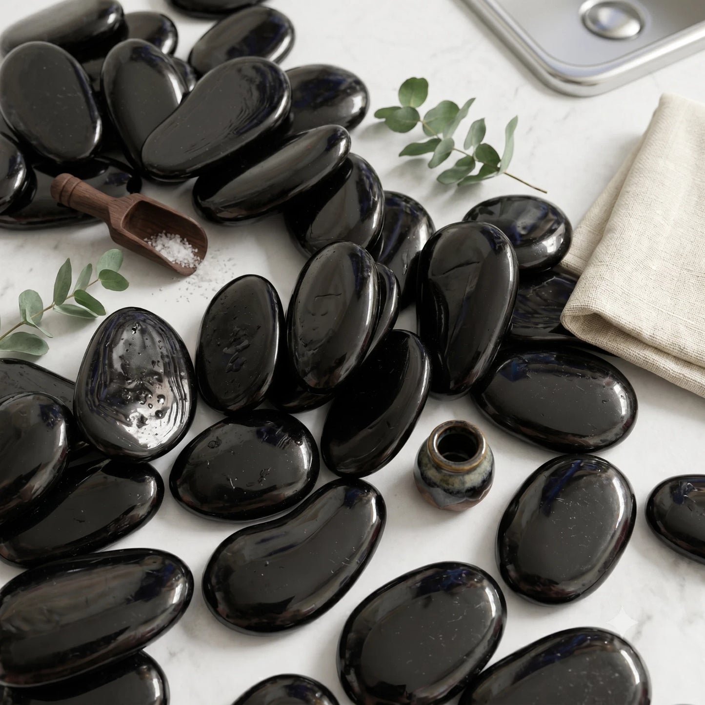 Black Polished Glass Decorative Pebbles arranged on a white surface with small green leaves and spa accessories SGI Online