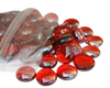 Red glass pebbles spilling out of a clear plastic bag by STONED glass pebbles vendor
