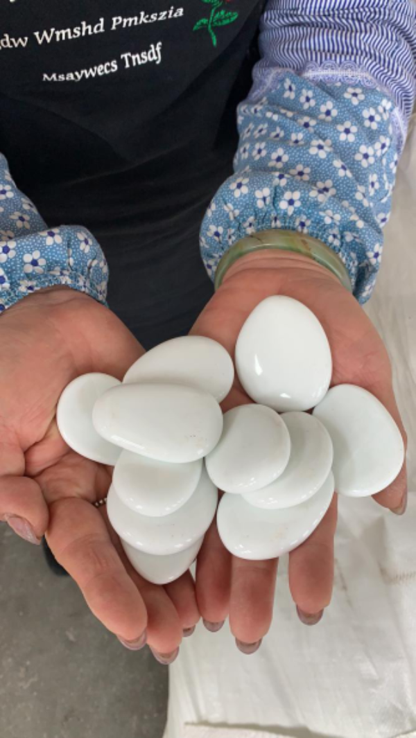 Hands holding smooth white story painting pebbles from SGI Online with blue floral sleeves